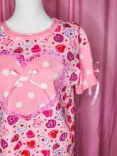 Load image into Gallery viewer, Pink t-shirt with heart cake patterns on a mannequin against a pink curtain background