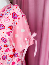 Load image into Gallery viewer, Pink shirt with heart cakes and polka dot sleeves with pink satin ribbon bows against a pink curtain.