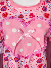 Load image into Gallery viewer, Pink t-shirt with white polka dots and a bow on a pink background with heart patterns