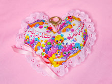 Load image into Gallery viewer, A heart-shaped fabric pouch featuring a colorful Popples print, finished with a gold key ring and a pink ribbon, set against a solid pink background.