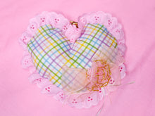 Load image into Gallery viewer, A handmade heart-shaped fabric ornament with a pastel plaid pattern, pink lace trim, and a small pink bow, displayed on a solid pink background.