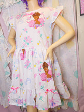 Load image into Gallery viewer, A short-sleeve white dress with a colorful cartoon ballerina print, musical notes, and floral motifs, displayed on a mannequin in front of a matching pastel fabric backdrop.