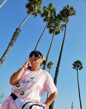 Load image into Gallery viewer, model wearing pink shirt with palm trees in background