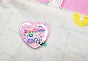 holographic heart pin that says "miss alphabet" with pink boombox and pillows