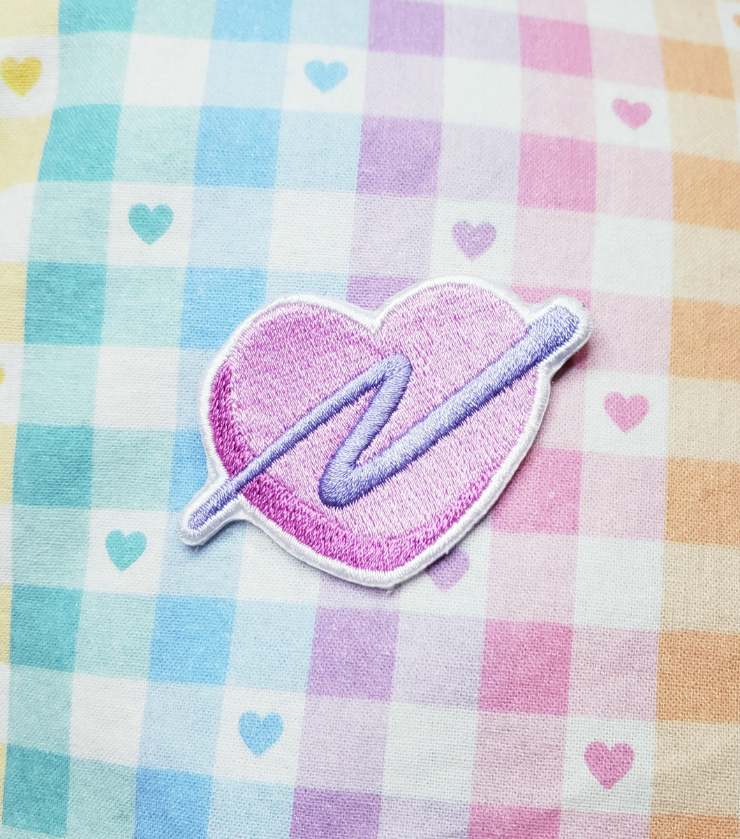 embroidered pink heart patch with purple swoosh on a rainbow gingham background