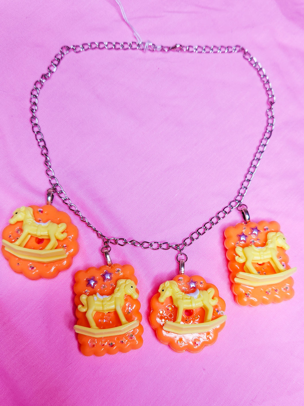 silver chain necklace with orange cracker biscuit charms with yellow rocking horses and rhinestones