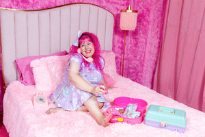 pink haired woman wearing a lavender crop top and skirt set with bone print, sitting in a pink room on a bed giving herself a pedicure