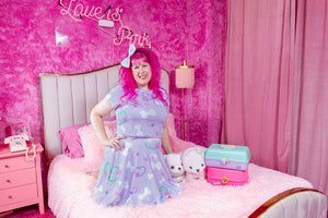 pink haired woman posing on a bed in a pink room wearing matching lavender crop top and skirt with bone print