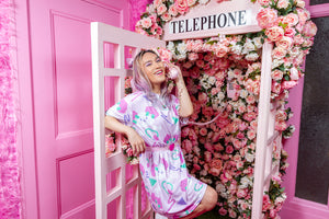 Asian woman wearing a pink dress with dog print, posing in a rose covered pink phone booth