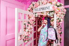 Load image into Gallery viewer, woman with bright colored hair posing in a rose covered pink phonebooth, modeling dog and bone print clothing