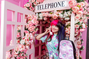 Caucasian woman wearing a mint green dress with dog print, posing in a rose covered pink phone booth