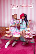 Load image into Gallery viewer, two pastel friends sharing a drink and desserts on a couch in front of a pink striped wall wearing dog print clothing